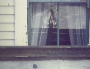 A blurry photo of a woman in window holding a 1970s camera