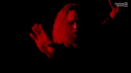 In dim red light someone dances with one hand facing out in front of them and one hand behind.