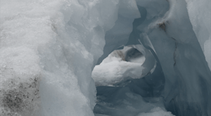 A white and pale blue ice cave holds fragments of dirt and smooth heavy ice.