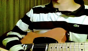 A pixelated image of a person holding a guitar wearing a long sleeve polo shirt, behind them are green curtains.