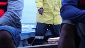 Three obscured figures ride in a boat over rough seas
