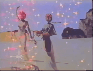 Overlaid VHS footage of two figures with rose's for heads hover on a beach are glittering intensely