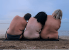 Three topless bodies sit in a line and rest against each other