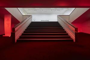 A classic cinema staircase is bathed in red light, at left a scroll of paper hangs down