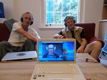 Mark Amery and Phil Dadson sit in a lounge smiling next to a laptop with Sean Kerr on a conference call