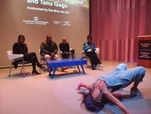 Four people sit a panel in the background whilst a performer in the foreground stretched their body across the floor