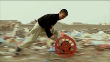 A young person runs through rubbish playing with a red wheel