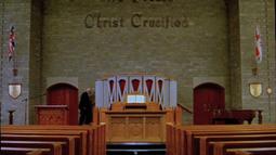 A person walks past the alter of a church, there are empty rows of pews in front. The Union Jack hangs off a back wall.