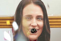A cardboard cut-out of Jacinda Ardern has had its eyes and mouth cut out. A confetti canister is poking out of her mouth, exploding glitter