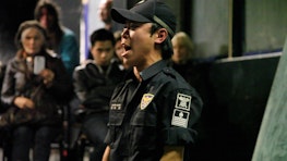 A person in military uniform appears to sing, shout or declaim while an audience quietly watch