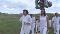 A group of people dressed in white walk through a field holding an inflatable sculpture by strings.