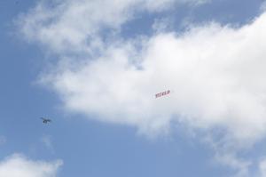 A plane flying in the blue skies toes a banner with the word SPECTACULAR in large red text