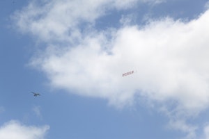 A plane flying in the blue skies toes a banner with the word SPECTACULAR in large red text
