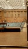 A large indoor pool with many people swimming. The walls are made of orange brick. Bright overhead lights shine down.