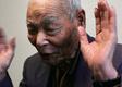 An older man raises his hands and closes his eyes whilst explaining something