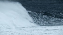 A still from Alex Monteith’s video work shows a large wave breaking. The ocean is a dark blue and foamy white.