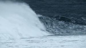 A still from Alex Monteith’s video work shows a large wave breaking. The ocean is a dark blue and foamy white.