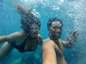 An underwater photo of two people smiling and waving happily with bubbles everywhere