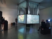 An art installation featuring a central square object onto which animated images are projected. Around the periphery audiences watch the different works.