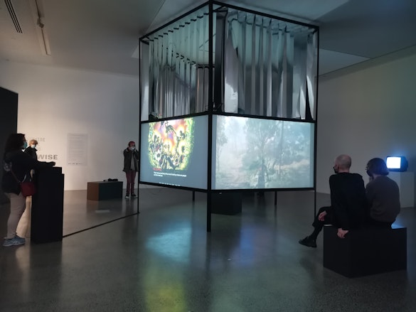 An art installation featuring a central square object onto which animated images are projected. Around the periphery audiences watch the different works.