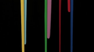 Against a black void background, long paint drips lines of yellow, teal, green, musky pink, blood red and navy blue.