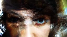 A person close to the camera stares down the lens, blue and yellow hues highlight their face.