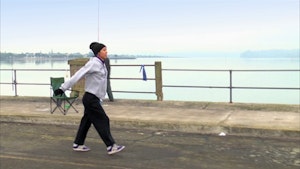 A person in a tracksuit and beanie dances along a bridge.