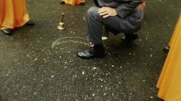 A man wearing a suit kneels down while drawing on the pavement.