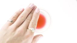 A hands touches the rim of a wineglass, there is a little bit of red wine left in the glass.