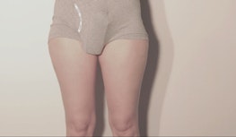 A pair of legs wearing beige underwear with an object wedged underneath the underwear creating a large bulge