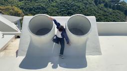 A person climes on a roof between to circular skylights.