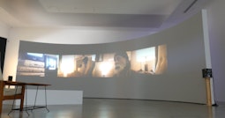 A large semi-circular wall in a gallery with videos projected on it.
