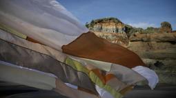 A thin patchwork cloth blows in the wind on the beach. Tall cliffs stand in the distance.