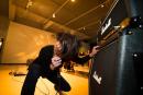 A person headbanging is singing into a microphone squatting down, holding onto the speaker