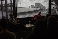 Mark Williams and Peter Wareing sit in front of three large screens displaying Peter's work in conversation.
