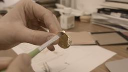 A hand carefully brushes gold leaf onto a handmade coin.
