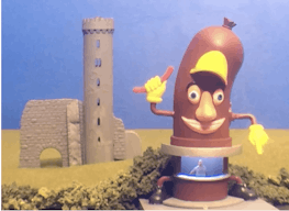 A model showing a small castle in the background and a giant sausage in the foreground with a person standing inside.