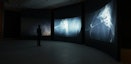 A darkened gallery with a curved wall shows three channel video work flightdream
