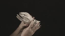 Two human hands hold a life-size figurine of hands that wear jewellery.