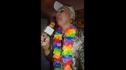 A person wearing a rainbow lei and gold hat sings into a golden microphone.