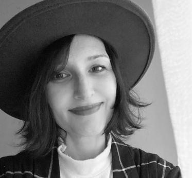 A black and white portrait photograph of a woman in a hat and checked blazer.