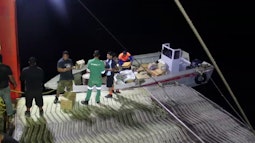 A group of people unload boxes from a small boat at night.