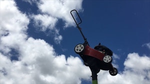 A lawn mower is suspended up a pole against a blue sky, it almost looks as if its flying through the air