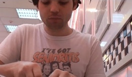Campbell sits in a booth at Burger King wearing a T-shirt that reads “I’ve got senioritis”. Behind him, the Burger King decor is black and white checkered tiles and framed photographs.