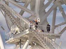 Workers stand on an immense steel structure wearing hardhats.