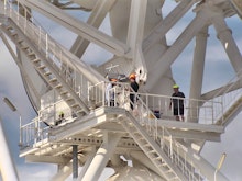 Workers stand on an immense steel structure wearing hardhats.