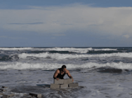A person is building a wall from concrete bricks in the ocean whilst waves crash nearby