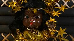 A brown children's doll is shrouded in gold stars and tinsel.