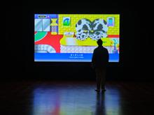 A silhouette stands near a large screen playing the work of Wong Ping