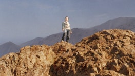 A double exposure photograph of a woman standing on a desert mountain, shot from below